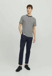 Camisa de mangas curtas às riscas, com riscas horizontais em azul-marinho e branco, combinada com calças azul-marinho e sapatos pretos, num fundo neutro.