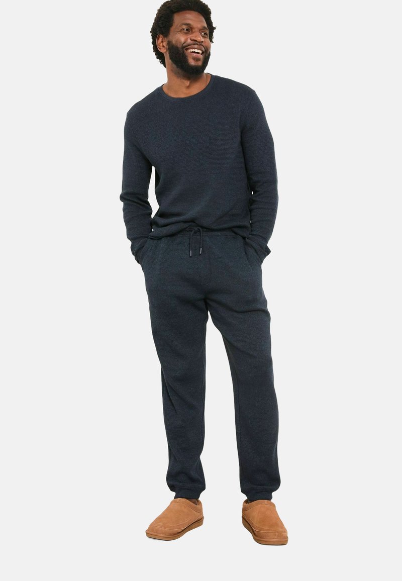 Marineblauer Strickpullover und passende Jogginghosen mit Kordelzug. Weicher Stoff; kombiniert mit beigen Slipschuhen. Lockere, bequeme Passform.