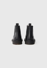 Mustad nahast pahkluu saapad paksude taldadega, tagant vaadatuna, ühevärvse valge taustaga.