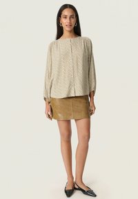 Blusa beige a pois con una vestibilità morbida e chiusura a bottoni, abbinata a una mini gonna in pelle color cammello. Le scarpe nere a punta completano il look.