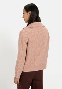 Roze gebreide cardigan met een geribde textuur en een brede kraag, voorzien van aansluitende manchetten en een cropped zoom, gestyled met donkere broek.
