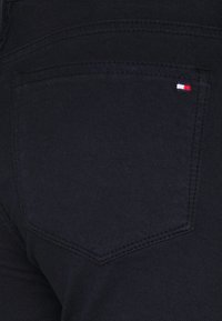 Jeans en denim noirs avec une poche arrière ornée d'un petit logo rouge, blanc et bleu. Tissu texturé avec une finition lisse.