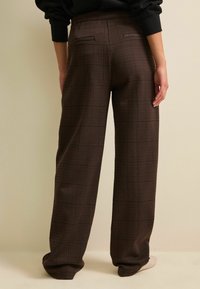 Pantaloni a quadri marroni con vita alta, dotati di tasche laterali e design ampio e rilassato. Tessuto liscio con una leggera texture.