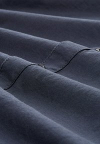 Tela de color azul marino oscuro con una textura suave, que presenta capas plegadas y costuras visibles. Incluye botones en el borde superior para añadir detalle.