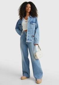 Chaqueta de mezclilla azul claro sobre un top corto blanco, combinada con jeans de pierna ancha, zapatos de plataforma y un pequeño bolso beige.