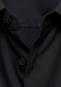 Cămașă de un albastru închis, realizată dintr-un material moale și texturat. Prezintă un guler ascuțit, două butoane negre și un design curat, fără modele vizibile.