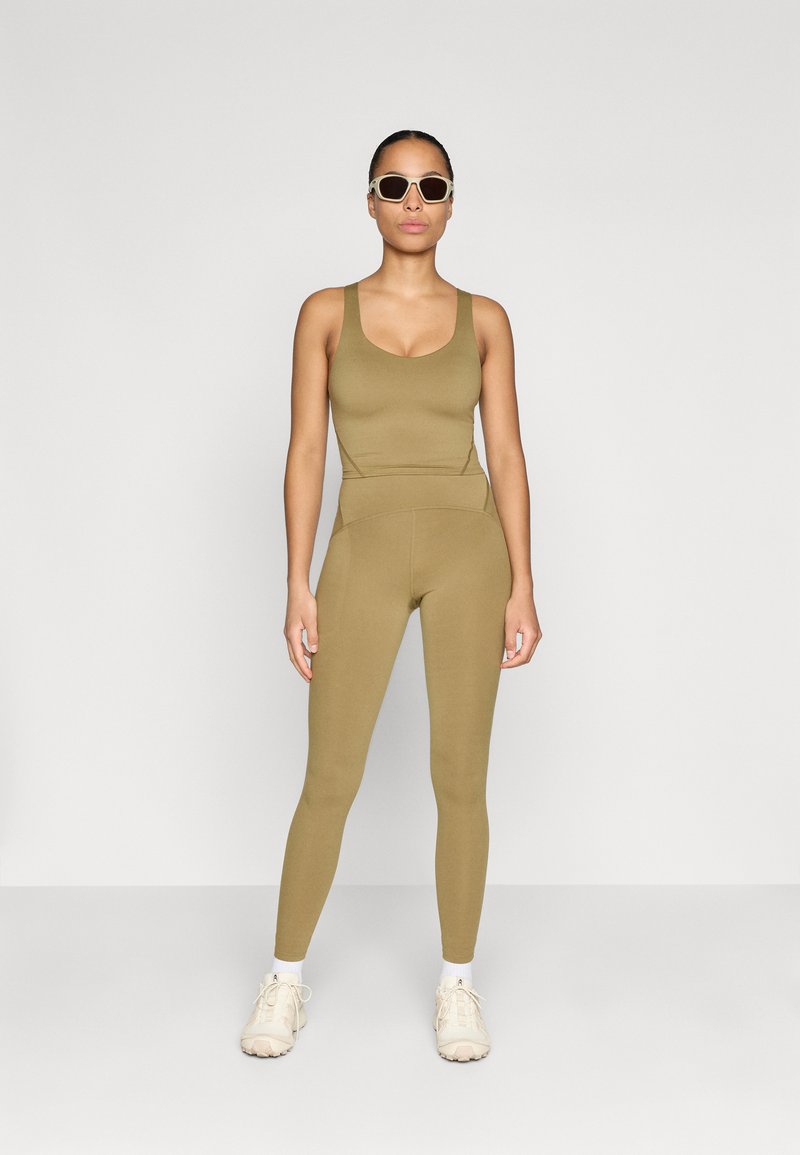 Olive green athletic set featuring a fitted tank top and high-waisted leggings, made of smooth, stretchy material. Worn with white sneakers.