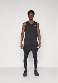 Black athletic tank top, shorts, and leggings; fitted, lightweight fabric; logo on tank; sleek design; paired with black sneakers.