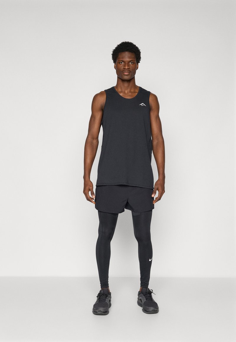 Schwarzes Sporttanktop, Shorts und Leggings; enganliegender, leichter Stoff; Logo auf dem Tanktop; elegantes Design; kombiniert mit schwarzen Sneakers.