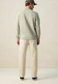 Lichtgroene gebreide sweatshirt met lange mouwen, gecombineerd met beige broek. De outfit heeft een eenvoudig ontwerp en een relaxte pasvorm, compleet met donkere schoenen.