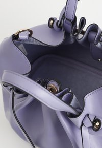 Borsa a mano viola in pelle con una texture morbida, parte superiore arricciata, hardware color oro e un ampio interno con una fodera liscia.