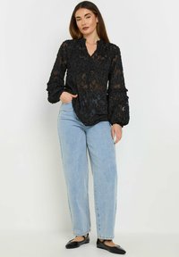 Zwarte doorschijnende blouse met bloemenborduursel, lange gerimpelde mouwen en een v-halslijn, gecombineerd met lichtblauwe high-waisted jeans en zwarte flats.