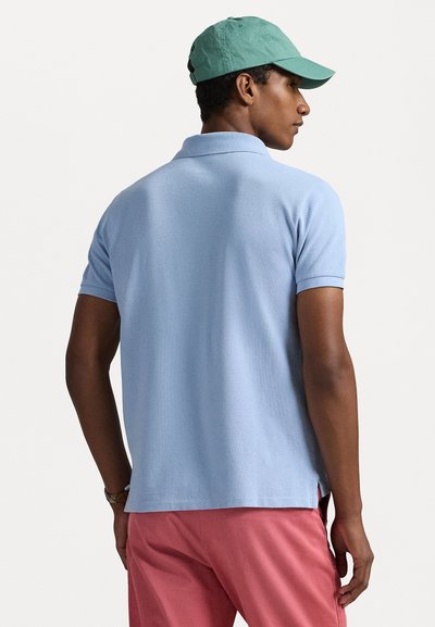 Light blue polo shirt with short sleeves and a ribbed collar, paired with pink shorts. The texture appears soft, with side slits at the hem.