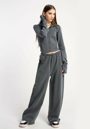 Szara kurtka typu zip w krótkiej wersji z długimi rękawami noszona z luźnymi szarymi spodniami dresowymi. Materiał ma miękką teksturę i casualowy design. Czarno-różowe trampki.