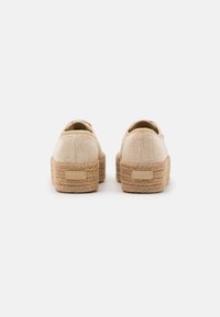 Baskets plateforme en toile beige avec semelles en jute tressé et une texture lisse, présentant un logo discret au niveau du talon et un design arrondi.