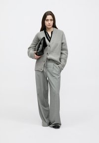 Gray knitted cardigan with buttons, paired with black blouse and gray wide-leg trousers. Model holds a black clutch bag.