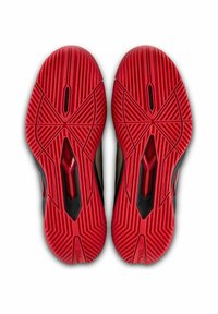 Rote und schwarze Sohlen von Sportschuhen mit einem strukturierten Grip-Muster, das diagonale Rillen und Aussparungen für die Traktion aufweist. Markenlogo sichtbar.