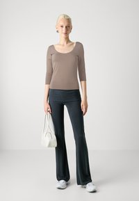 Brown fitted top with scoop neckline, 3/4 sleeves; dark flared pants; white handbag; white sneakers; smooth texture.