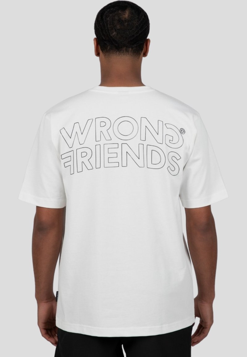 Bílý bavlněný tričko s velkým obrysem textu "WRONG FRIENDS" na zadní straně. Krátké rukávy a volný střih se rovnými lemy.