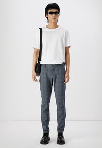 Graue Karohosen mit einem maßgeschneiderten Schnitt, kombiniert mit einem schlichten weißen T-Shirt und schwarzen Sonnenbrillen, accessoriert mit einer kleinen schwarzen Tasche.