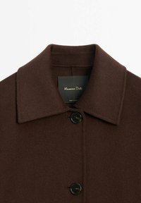 Brauner Wollmischungs-Mantel mit spitzem Kragen, einreihiger Knopfleiste und zwei schwarzen Knöpfen. Enthält ein Etikett mit Markennamen.