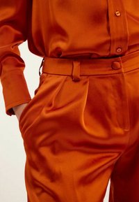 Ensemble chemise et pantalon en satin vibrant orange, avec une texture lisse, des détails de boutons, une taille élastique et des plis subtils dans le pantalon.