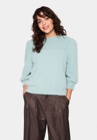 Light blue, fluffy sweater with a round neckline and three-quarter sleeves, paired with brown high-waisted pants. Soft texture, relaxed fit.
