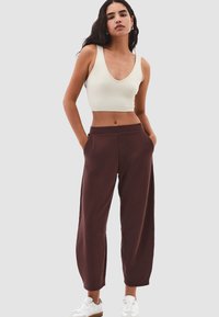 Bruine wijde broek gemaakt van zachte stof, met een hoge taille, zijzakken, en gecombineerd met een lichte tanktop en witte sneakers.