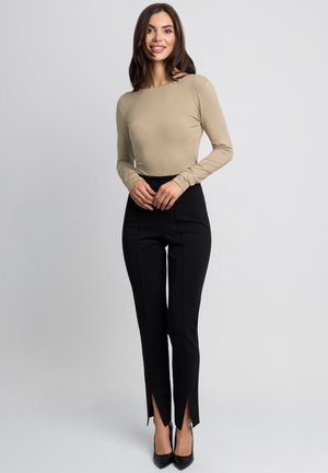 Beżowa bluzka z długim rękawem w połączeniu z czarnymi spodniami z wysokim stanem z bocznymi rozporkami, dopełnione czarnymi butami na wysokim obcasie.