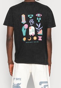 Svart T-shirt med en flerfärgad grafisk design på baksidan, inklusive händer, växter och geometriska former, i mjukt bomullstyg.