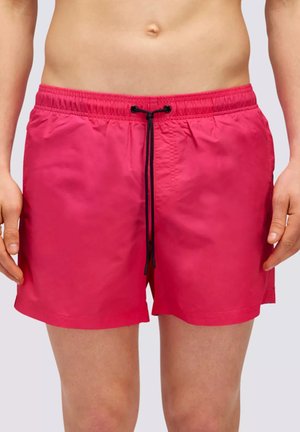 Uomo che indossa pantaloncini da bagno rosa acceso con coulisse nera, mostrato dalla vita a metà coscia su sfondo neutro.