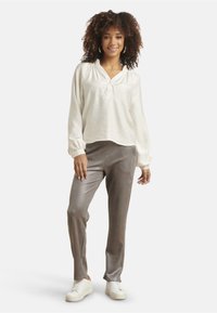 Lightweight ivory blouse with a V-neck, long sleeves and embroidered accents, paired with metallic gray trousers and white sneakers.
