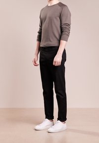 Maglietta grigia a maniche lunghe, pantaloni neri slim-fit e sneakers bianche. La maglietta ha un colletto tondo; i pantaloni presentano tasche laterali e una vestibilità classica.