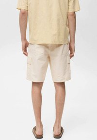 Beige cargoshorts met zijzakken en een relaxte pasvorm, gecombineerd met een lichtgele patronen blouse. Casual schoenen maken de look compleet.