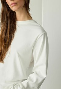 Biała bluza z okrągłym dekoltem i ściągaczami, wykonana z miękkiego materiału, charakteryzująca się luźnym krojem i gładką fakturą.