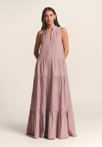 Robe maxi longue sans manches, à volants, de couleur mauve clair. Dotée d'une fermeture à boutons sur le devant et d'un tissu texturé froissé. Col arrondi.