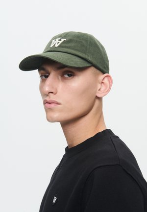 Jeune homme portant une casquette verte avec un logo blanc "W" et un sweat-shirt noir avec un petit emblème "W" assorti sur la poitrine.