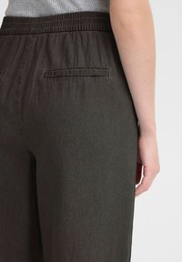 Pantalons élastiques gris foncé avec une texture lisse, dotés de deux poches au dos et d'une coupe décontractée. Design simple et fonctionnel.