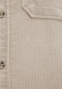 Beige Kordhemd mit vertikalen Streifen, einer Klappentasche und Knopfverschluss. Weicher Stoff mit runden Knöpfen.