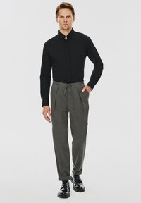 Czarna koszula z guzikami, szare spodnie z troczkami i czarne buty. Gładki materiał, dopasowany krój, z podwiniętymi nogawkami i plisowanym wzorem.