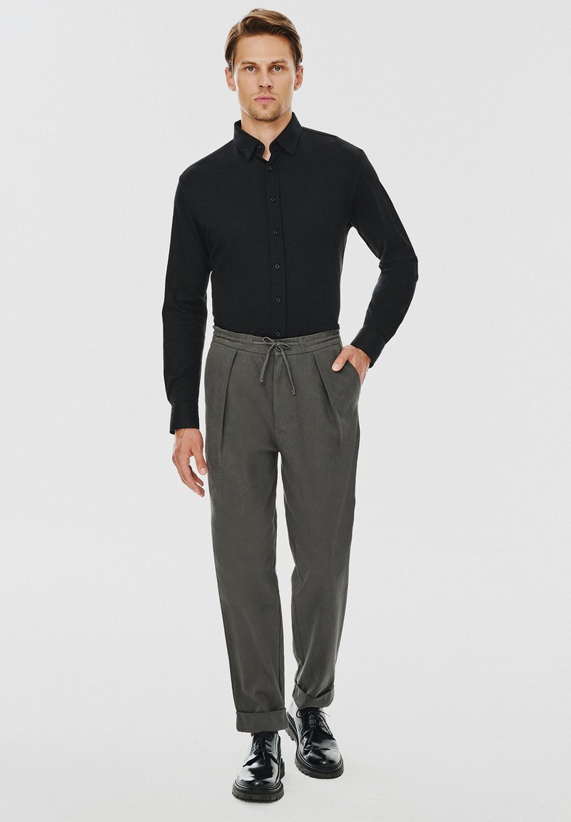 Czarna koszula z guzikami, szare spodnie z troczkami i czarne buty. Gładki materiał, dopasowany krój, z podwiniętymi nogawkami i plisowanym wzorem.