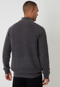 Suéter gris de punto acanalado con cuello alto y mangas largas, que presenta un corte holgado y un dobladillo y puños acanalados.