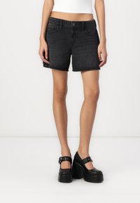 Shorts en denim noir avec un ourlet effiloché, comportant des poches avant et une fermeture à bouton. Assortis avec des chaussures à talons noires avec des brides de cheville.