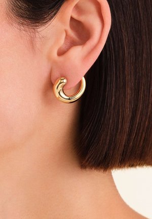 Gouden oorring in de vorm van een gladde, gebogen hoepel. Het reflecterende oppervlak heeft een gepolijste afwerking, waardoor de ronde vorm en stijl extra benadrukt worden.