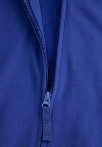 Niebieska tkanina z zamkiem błyskawicznym w zbliżeniu, o gładkiej fakturze i kontrastowych detalach zamka. Materiał wydaje się miękki i elastyczny.