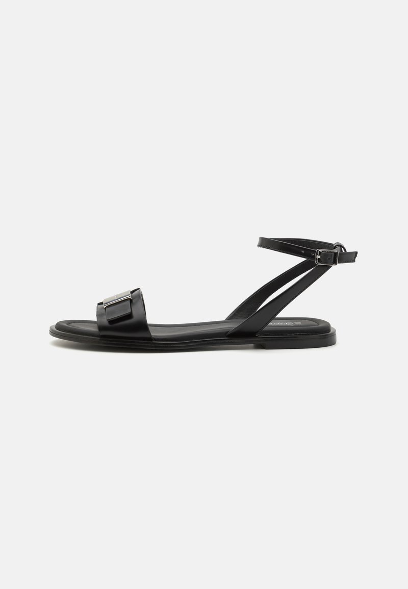 Black flat sandals with a simple strap design, a square accent on the front, and an ankle strap secured with a buckle. Smooth texture.