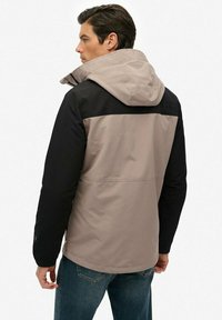Herrejakke med hætte, farveblokeret design med sorte ærmer og en beige krop, lavet af et glat, vejrbestandigt stof.