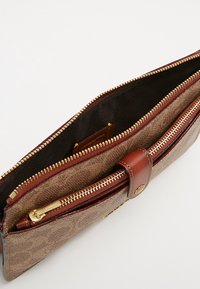 Brązowa torebka kopertówka z złotymi akcentami, z zamknięciem na zamek błyskawiczny, kontrastowym ciemnym wnętrzem oraz zewnętrzną kieszenią na przechowywanie.