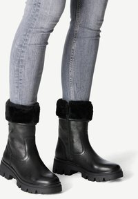 Bottes de cheville en cuir noir avec une finition texturée, un revers en fourrure et une semelle en caoutchouc épaisse. Détail zippé sur le côté pour une fonctionnalité améliorée.