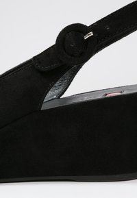 Sandale compensée en suede noir avec un accent de sangle circulaire et une boucle ajustable. Présente un design épuré avec une surface texturée.